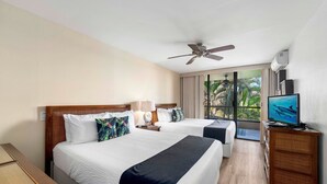 Ein Hotelzimmer mit zwei Betten, einem Deckenventilator, einem Fernseher und Blick auf Palmen durch das Fenster.
