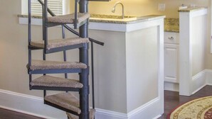 A spiral staircase with a cat tree, a kitchen area with white cabinets, and a small island with a sink. - HISTORIC DISTRICT ~ Walk Everywhere ~ Private Parking! (St. Augustine)