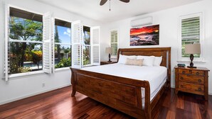 Ein Schlafzimmer mit einem hölzernen Bett, weißen Wänden und großen Fenstern mit Rollläden.