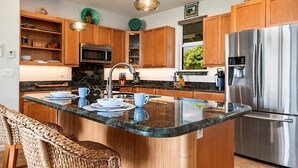 Eine moderne Küche mit Holzausstattung, einem Edelstahlkühlschrank, einer eingebauten Mikrowelle und einer Arbeitsplatte aus Granit.
