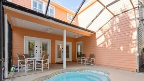 Un jardín trasero con piscina, muebles de patio blancos y un área de patio techada.
