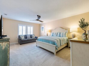 A bedroom with a bed, a sofa, a television, and a ceiling fan.