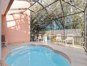 A covered outdoor swimming pool with a wooden deck, surrounded by white chairs and a fence.