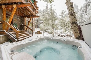 Un bain à remous installé dans un cadre extérieur enneigé, avec une terrasse en bois et un escalier menant à un bâtiment.