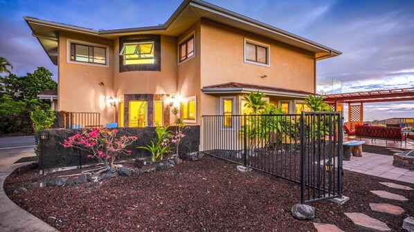 A two-story house with a landscaped garden, a patio with outdoor furniture, and a view of the ocean. - 🏖️Kona Private Home w/ A/C, Pool & Rooftop Ocean Views (Kailua Kona)