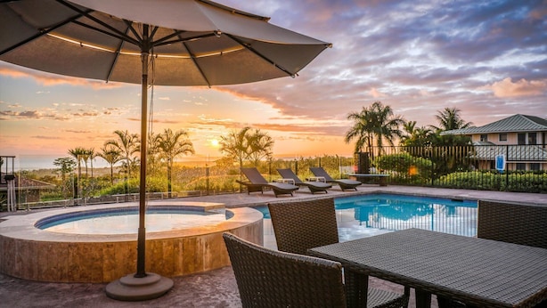 A pool area with lounge chairs and a hot tub, surrounded by palm trees and a view of the sunset.