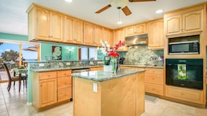 A kitchen with wooden cabinets, a granite countertop, a built-in microwave, and a ceiling fan.
