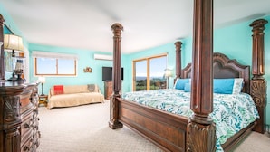 A spacious bedroom with a large bed, a smaller sofa, and a dresser. There is a window providing a view of the outdoors.