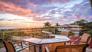 A balcony with a glass railing overlooking a swimming pool and a view of a house with a green roof.