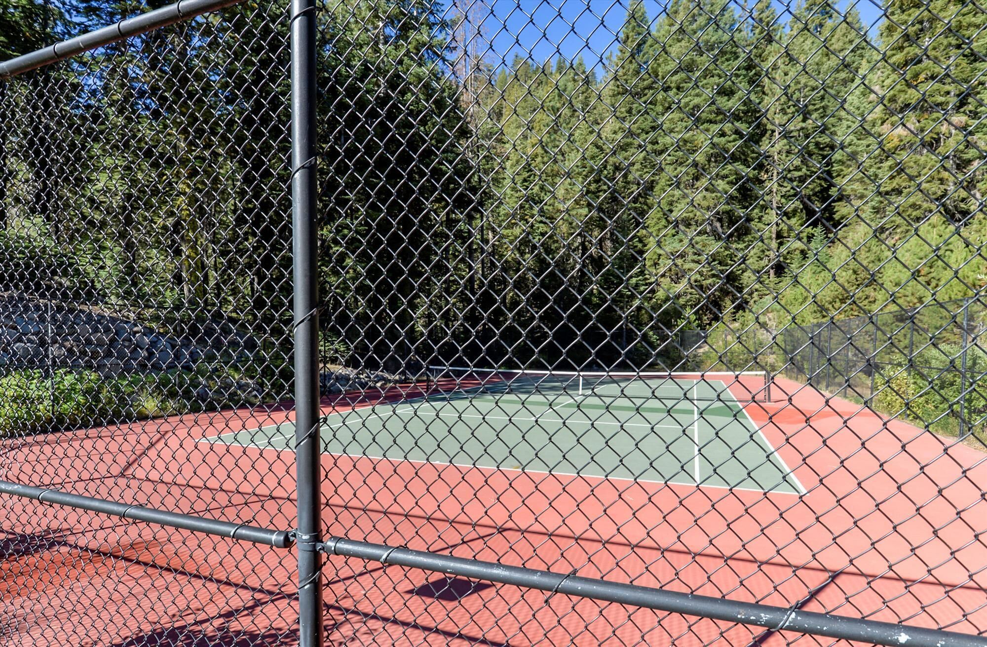 A tennis court enclosed by a chain-link fence with a metal pole in the foreground.