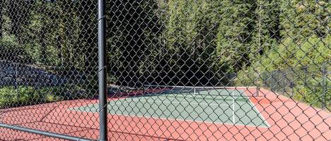 A tennis court enclosed by a chain-link fence with a metal pole in the foreground.