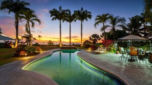 Piscina com vista para o pôr do sol, cercada por palmeiras e área de estar ao ar livre.