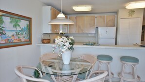 A kitchen with white cabinets, a white refrigerator, and a hanging light fixture. - 🏖️Oceanfront Kona Condo | Ground Floor, No Stairs (Kailua-Kona)