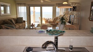 A kitchen with a modern faucet, a glass dish rack, and a view of the ocean through a sliding glass door. - 🏖️Oceanfront Kona Condo | Ground Floor, No Stairs (Kailua-Kona)