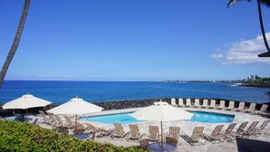 A poolside area with lounge chairs and umbrellas, overlooking the ocean. - 🏖️Oceanfront Kona Condo | Ground Floor, No Stairs (Kailua-Kona)