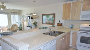 A kitchen with a dishwasher, sink, and white cabinets. - 🏖️Oceanfront Kona Condo | Ground Floor, No Stairs (Kailua-Kona)