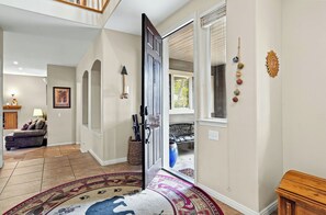 A spacious hallway with a patterned rug, a door leading to a room with a large window, and a small table with a vase.