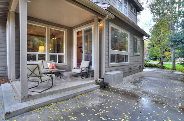 A covered porch with outdoor seating, a radiator, and a tree in the background.