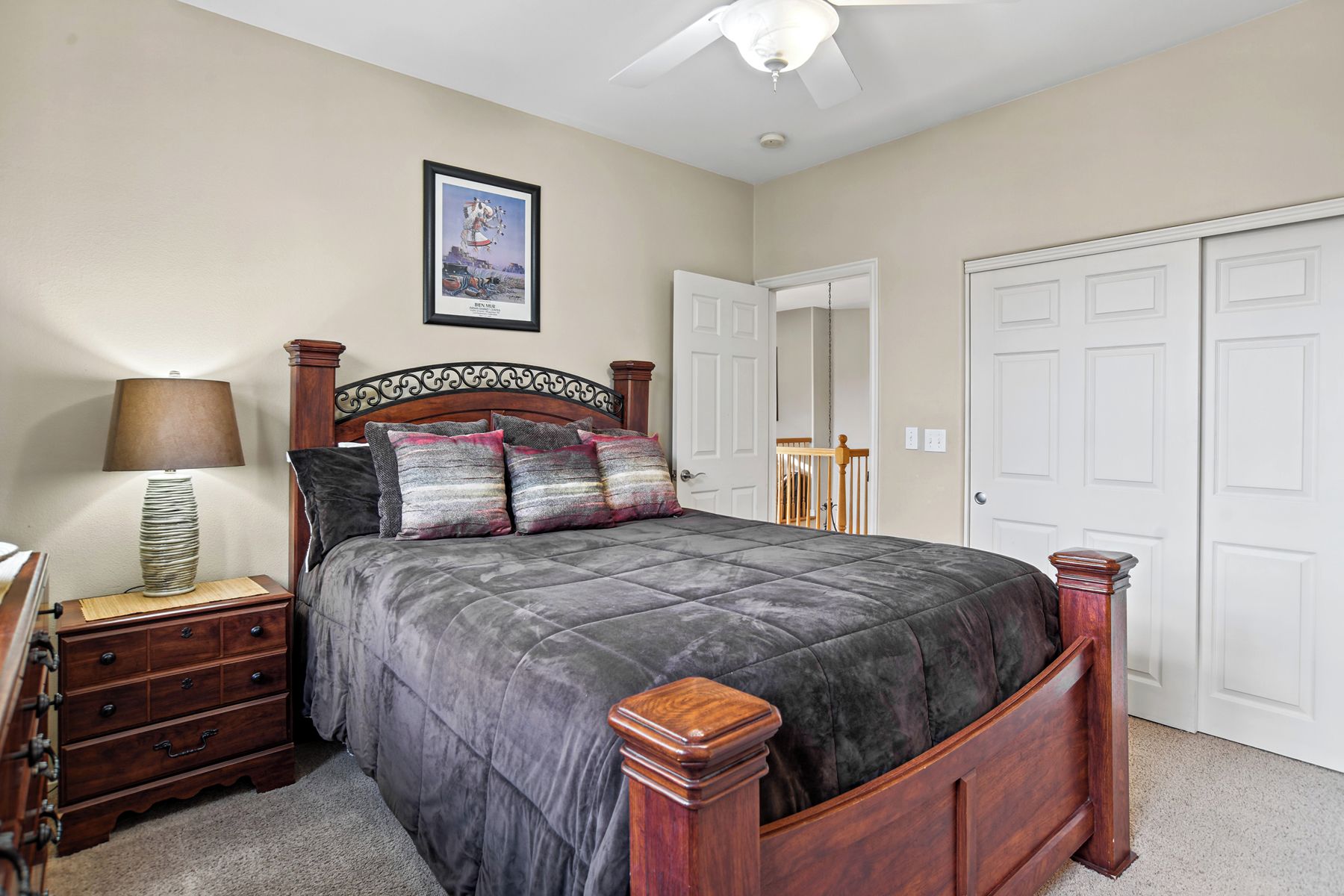 A bedroom with a bed, a nightstand, a lamp, a framed picture on the wall, and a ceiling fan.