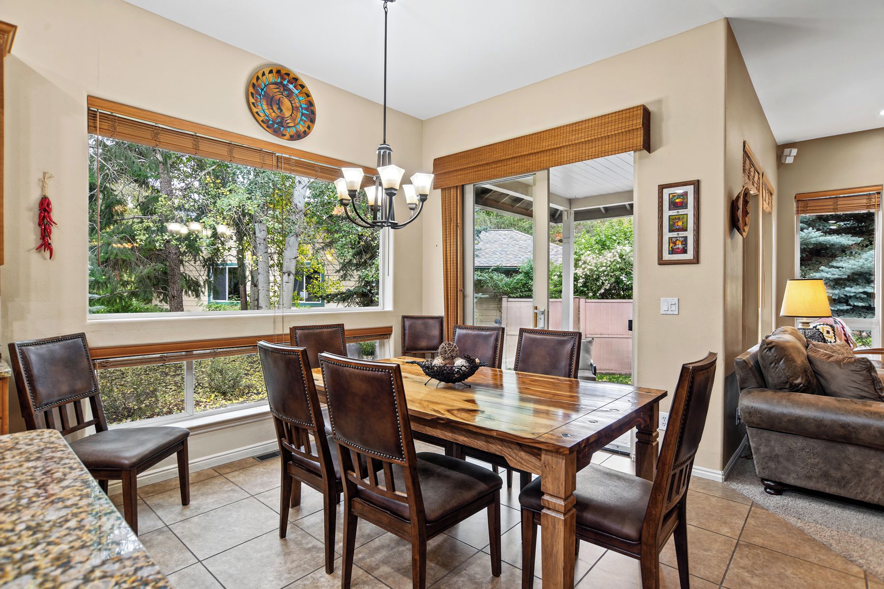 A dining area with a wooden table and chairs, large windows with a view of trees, and a chandelier.