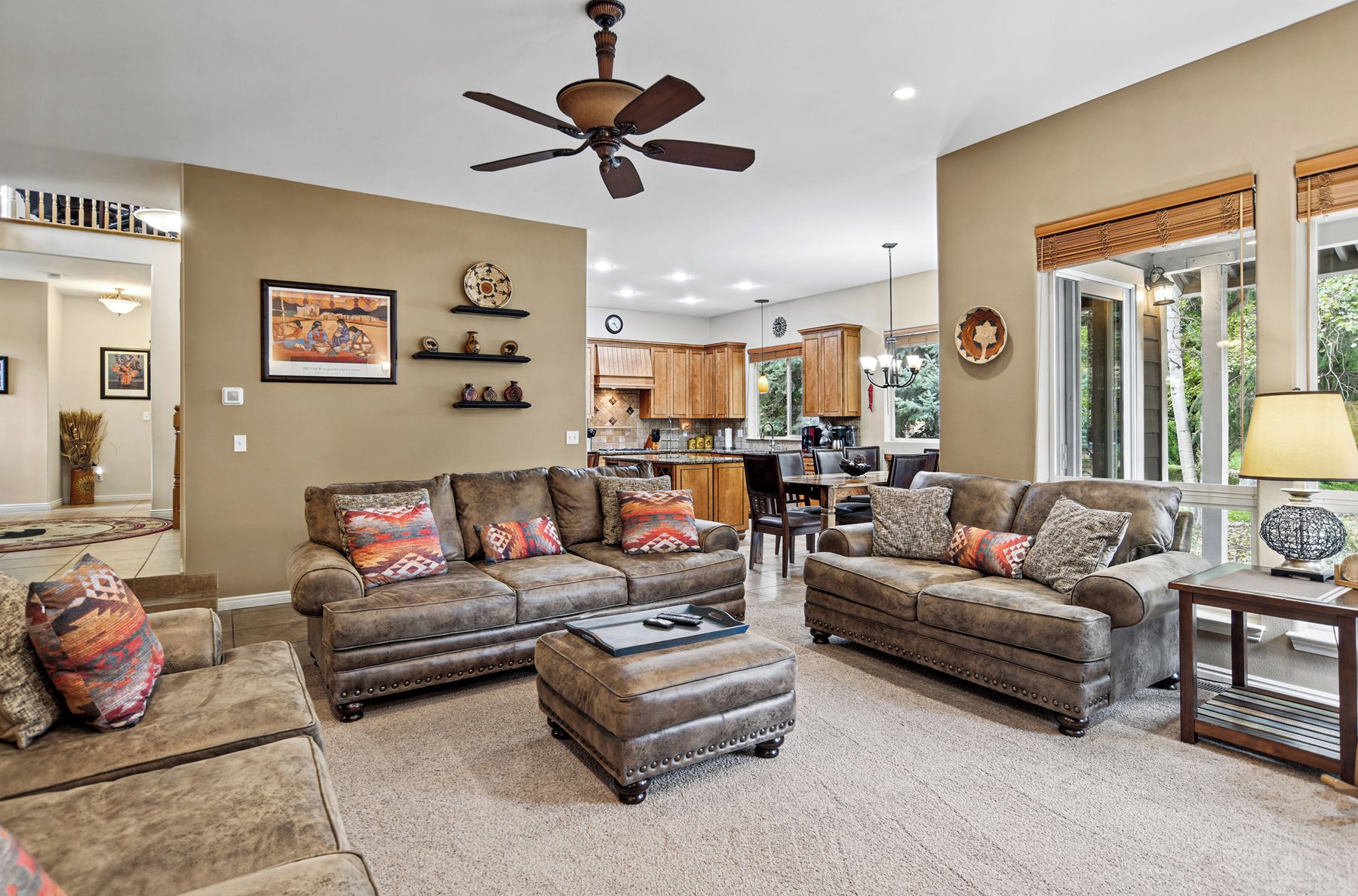 A spacious living room with leather sofas, a coffee table, and a ceiling fan.