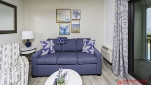 A living room with a blue sofa, patterned cushions, a round coffee table with a plant, and framed artwork on the wall. - Million Dollar Views ~ Heated Pool ~ King Bed (St Augustine)