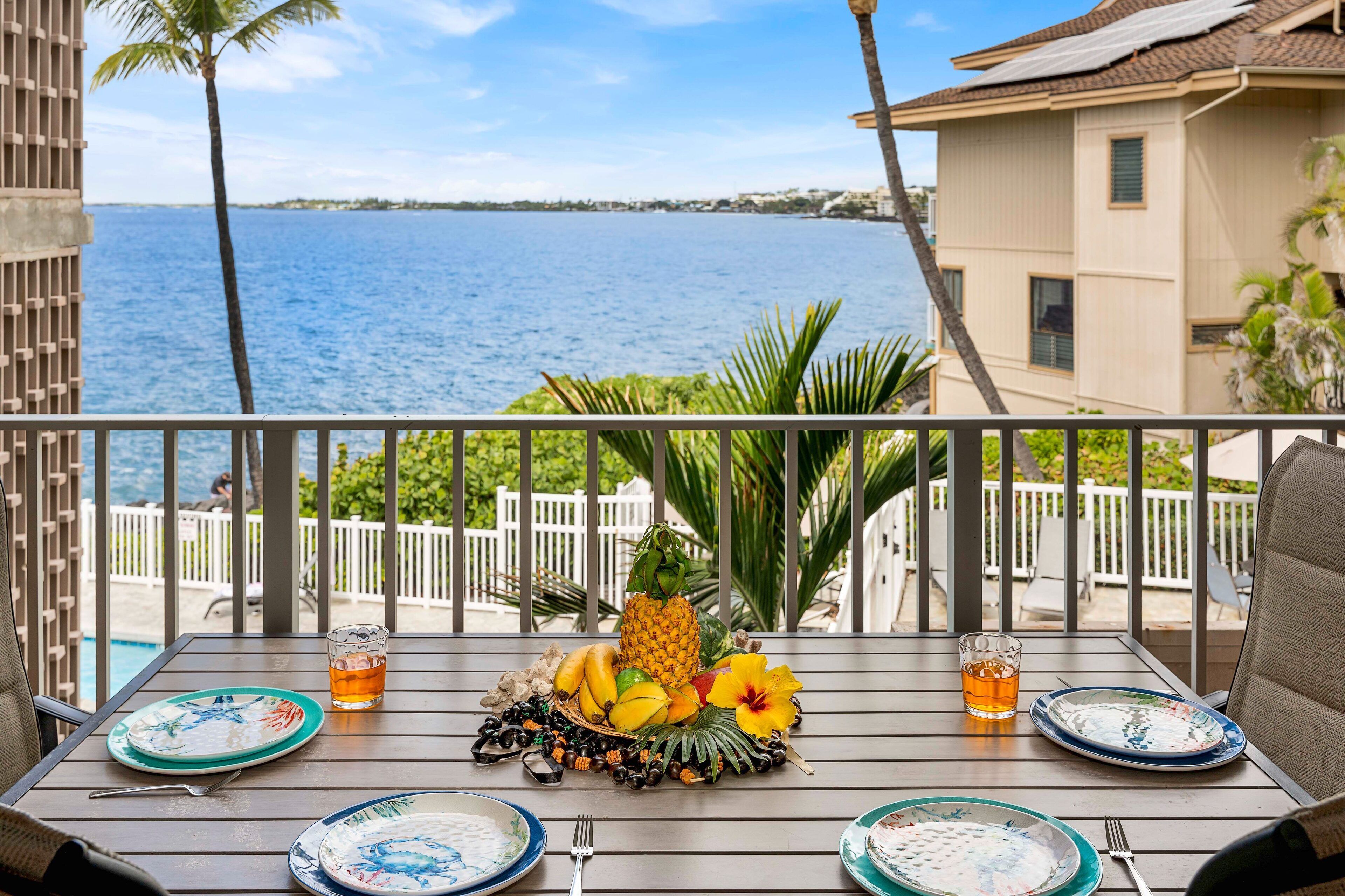 A balcony with a table set for two, overlooking a beach and ocean.