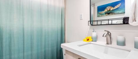 A bathroom with a shower curtain, toilet, sink with a mirror above, and a towel rack.