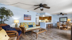 A living room with wicker furniture, a glass coffee table, and a ceiling fan.