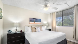 A bedroom with a bed, nightstands, a ceiling fan, a painting, and a window with blinds.