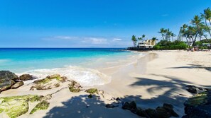 A beach with clear turquoise water, sandy shore, and a building with a balcony overlooking the sea.