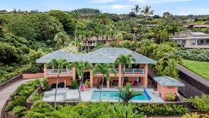 Una amplia casa con piscina, rodeada de exuberante vegetación y palmeras.