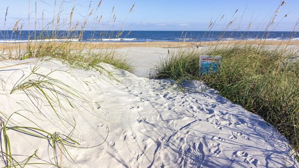 Een zandstrand met voetafdrukken en hoog gras.