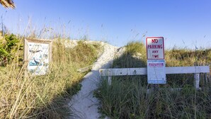 Een strandtoegang met een bord waarop staat 'Parkeren Verboden' en een houten hek.