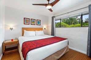 Une chambre d’hôtel avec un lit, une table de chevet, un ventilateur de plafond et une fenêtre avec des rideaux.