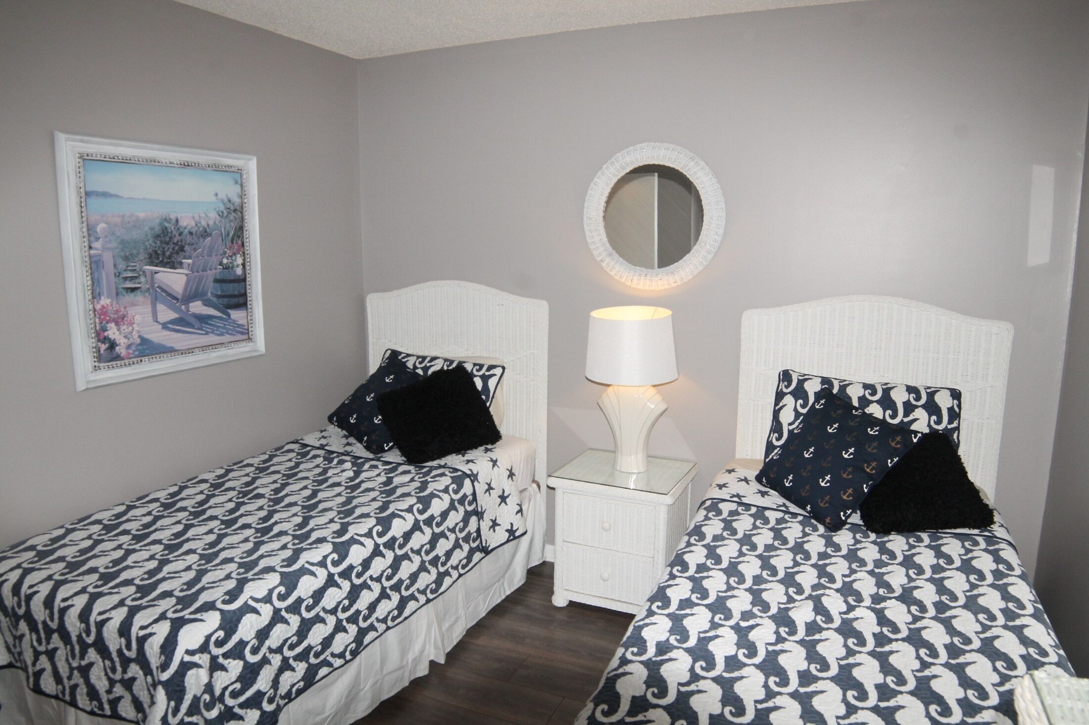 A bedroom with two beds, each with a patterned bedspread, a bedside lamp, a mirror, and a framed picture on the wall.