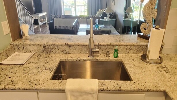 A kitchen with a granite countertop, stainless steel sink, and white cabinets. - Sea Place 13239:  Charming Beach Condo: 2 Bedrooms, Pools & Tennis Courts (St. Augustine)
