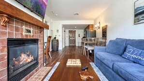 Una sala de estar con chimenea, un sofá azul y un área de comedor al fondo.