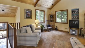 Ein gemütliches Wohnzimmer mit Holzboden, einer Couch, einem Schaukelstuhl, einem Fernseher und einem Kamin.