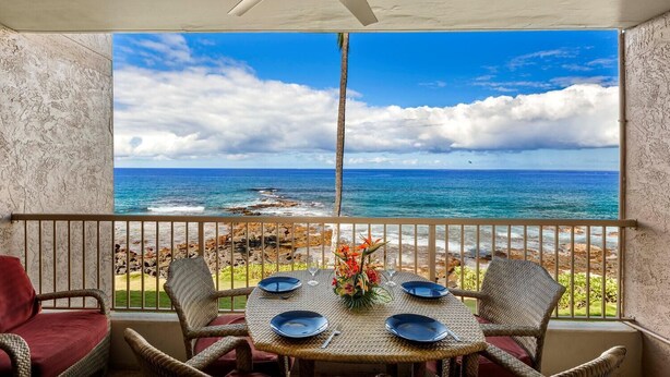 Een balkon met een tafel gedekt voor twee, met uitzicht op een rotsachtige kustlijn en de oceaan.