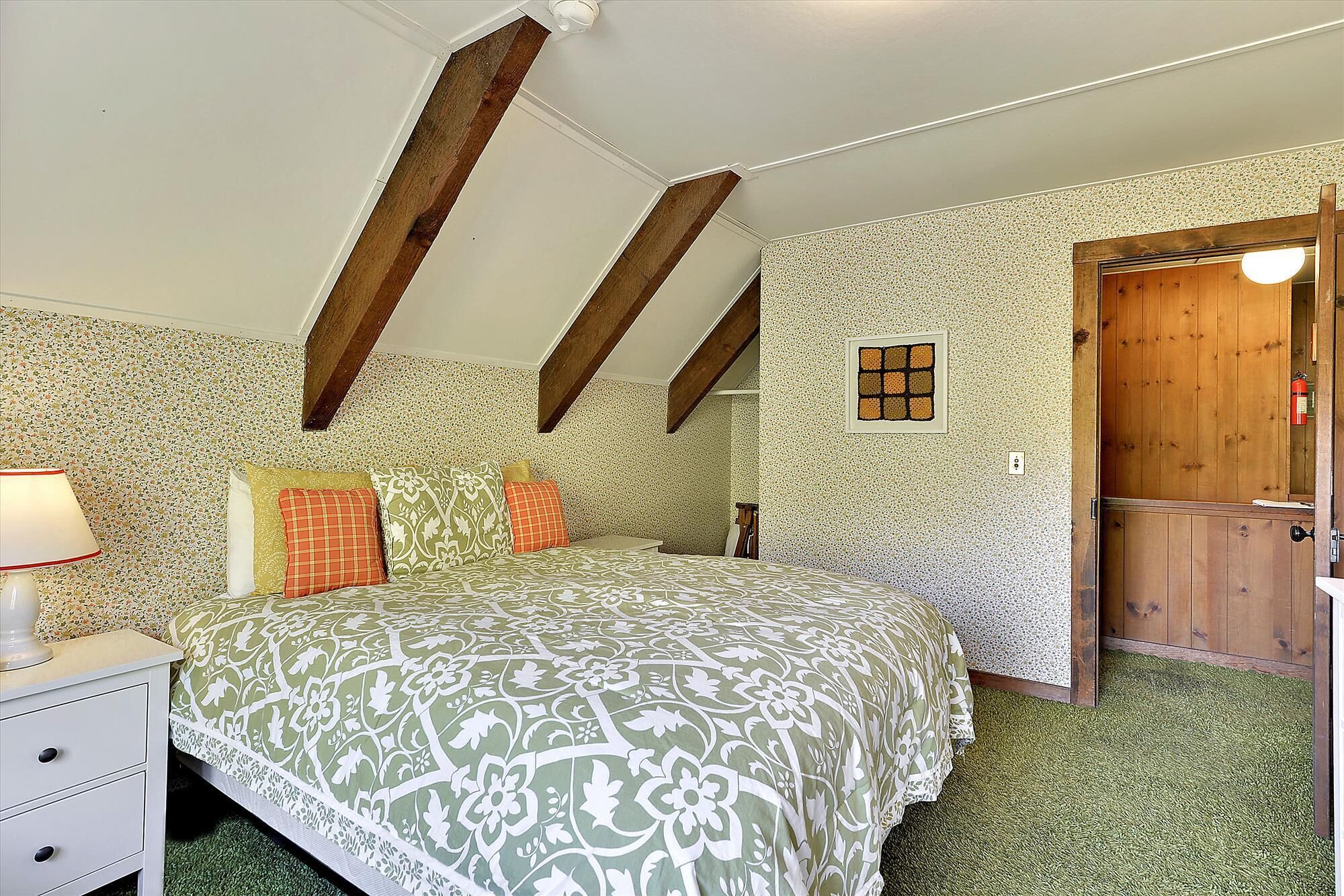 A bedroom with a bed, a nightstand, a wooden door, and a textured wall.