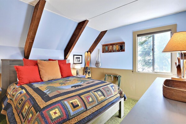 A bedroom with a large bed, a window with a view, and a lamp on a bedside table.