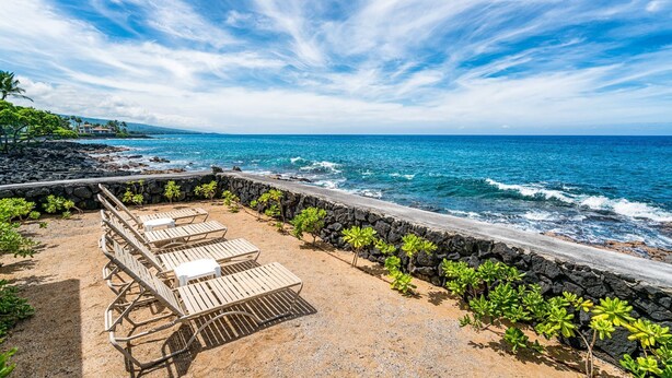 A beachside patio with lounge chairs and a stone wall overlooking the ocean.