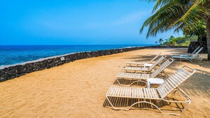 A beach with white lounge chairs and a stone wall.