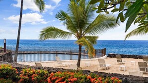 A beachside view with a pool, palm trees, and lounge chairs.