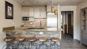 A kitchen with a stone island, bar stools, a refrigerator, and wooden cabinets. - Managed by Park City Lodging-On Main Street-Walk to Lift-Rooftop Deck-Views (Park City)