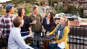 A group of people seated around a table outdoors with a scenic view of a town in the background. - Managed by Park City Lodging-On Main Street-Walk to Lift-Rooftop Deck-Views (Park City)