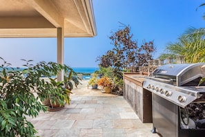 An outdoor patio with a grill, potted plants, and a view of the ocean.