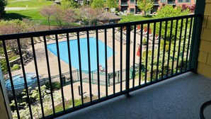 Blick auf einen Poolbereich mit umzäunter Terrasse, Liegestühlen und einem Gebäude im Hintergrund.