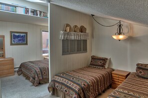 Une chambre avec deux lits, une commode, une table de chevet, un luminaire suspendu, une fenêtre avec des volets et une bibliothèque.